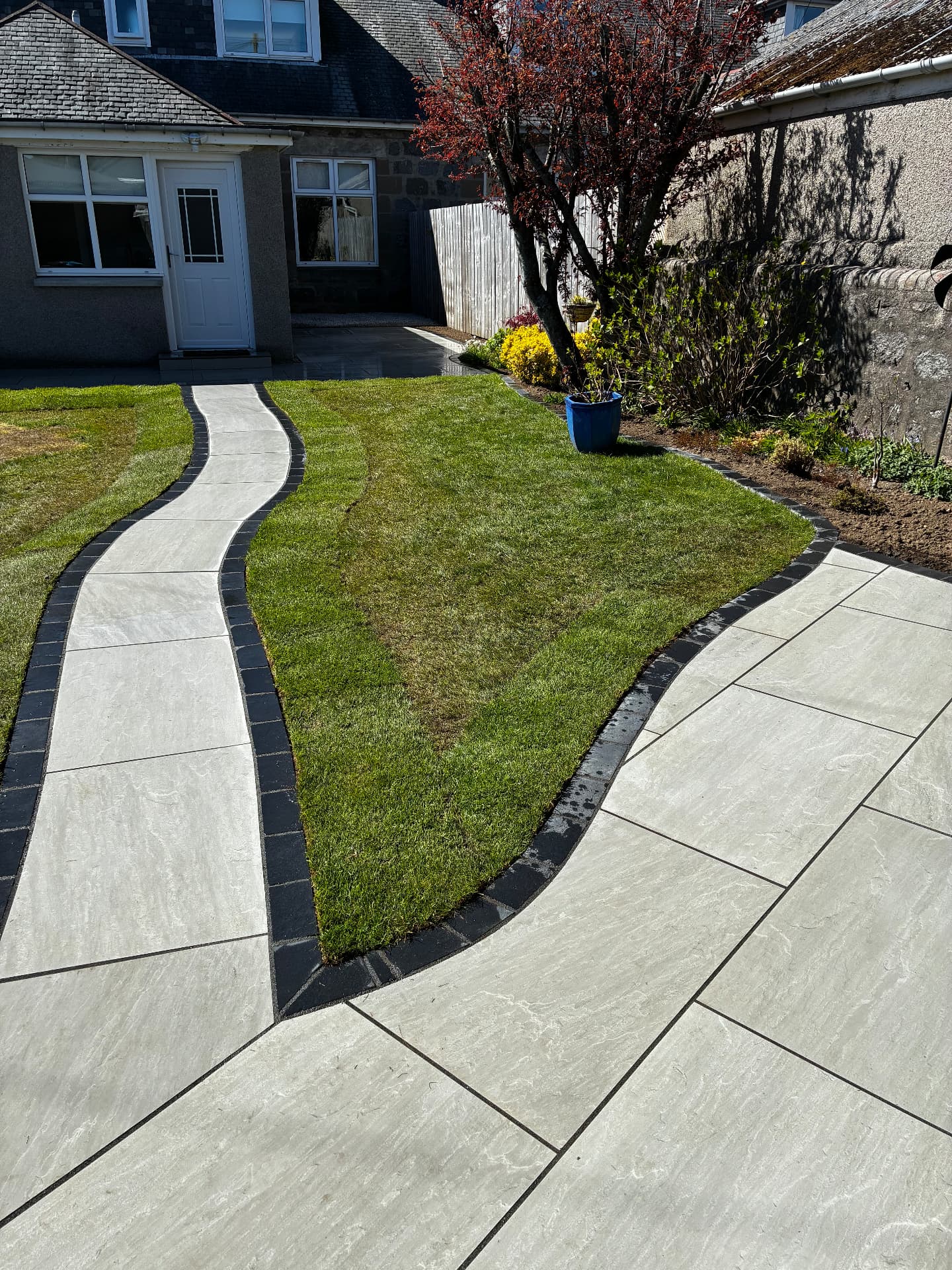 Curved Kandla grey porcelain path with black limestone setts through a lawn in Aberdeen